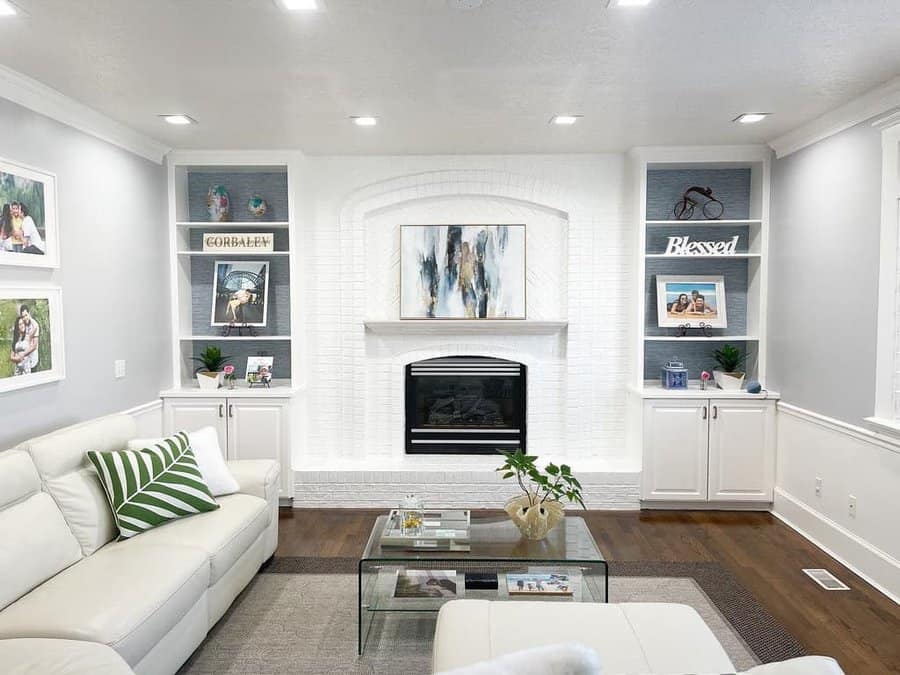 Modern living room with a white brick fireplace, abstract art, and shelves displaying decor; white sofa with green-striped pillow