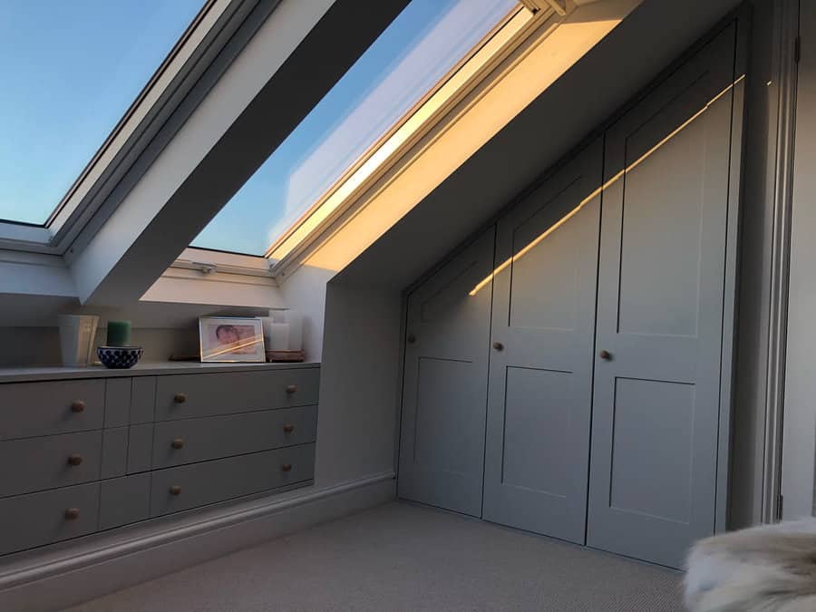 Attic storage with built-in wardrobes and drawers under a sloped ceiling, illuminated by large skylights for a bright and airy feel.