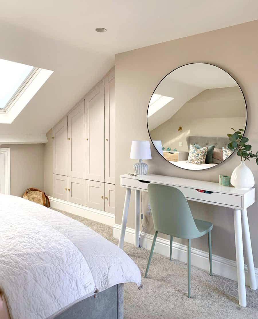 Elegant attic bedroom with built-in wardrobes under a sloped ceiling, a skylight, and a modern vanity with a round mirror.