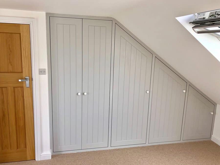 Custom-built grey fitted wardrobes under a sloped attic ceiling, maximizing storage space with a clean and functional design.