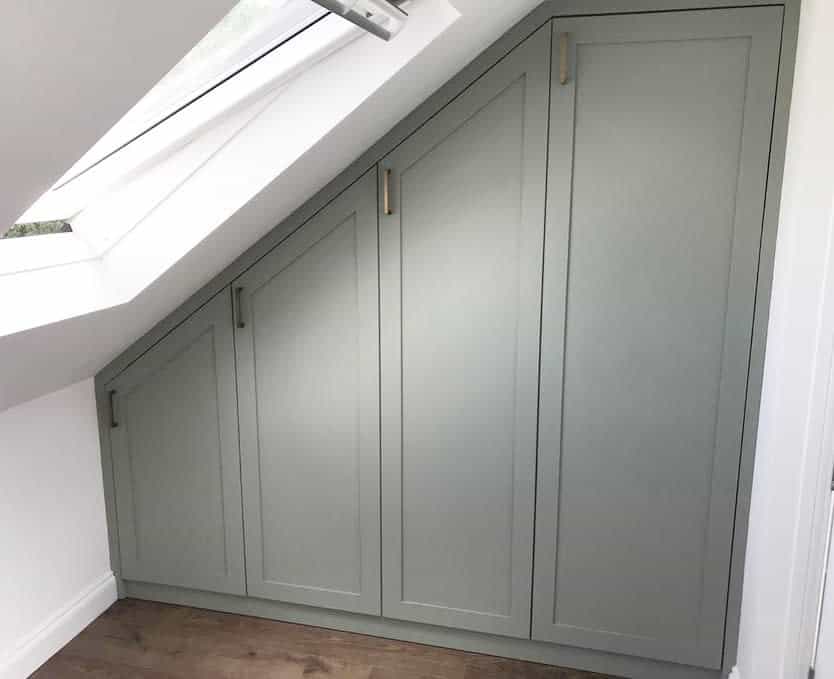 Custom-fitted sage green wardrobes under a sloped attic ceiling, maximizing storage with a sleek design and skylight for natural light.