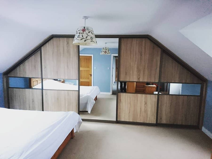 Custom attic wardrobe with wood and mirrored sliding doors, maximizing storage while complementing the sloped ceiling design.