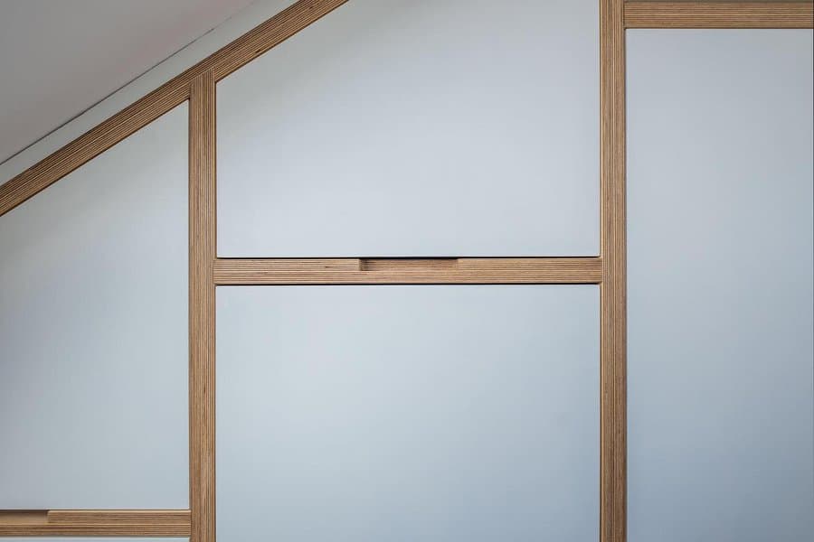 Modern fitted attic wardrobe with geometric wood framing and sleek white panels, designed to maximize storage under a sloped ceiling.