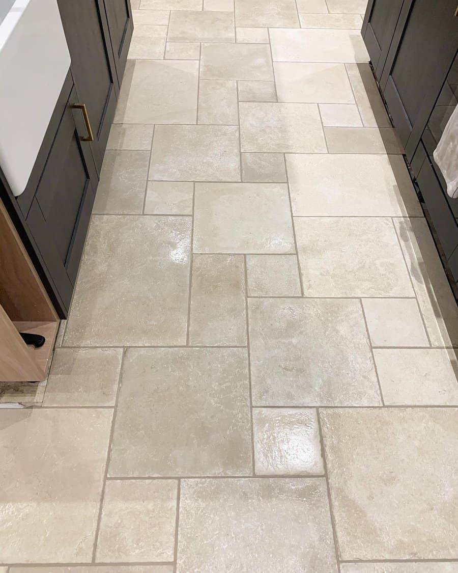 A kitchen with beige rectangular and square tiles on the floor, surrounded by dark cabinets