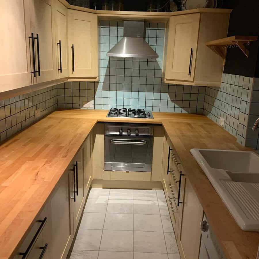 Light square tile flooring brightens this U-shaped kitchen, complementing wood countertops and soft cabinetry for a cozy, rustic charm