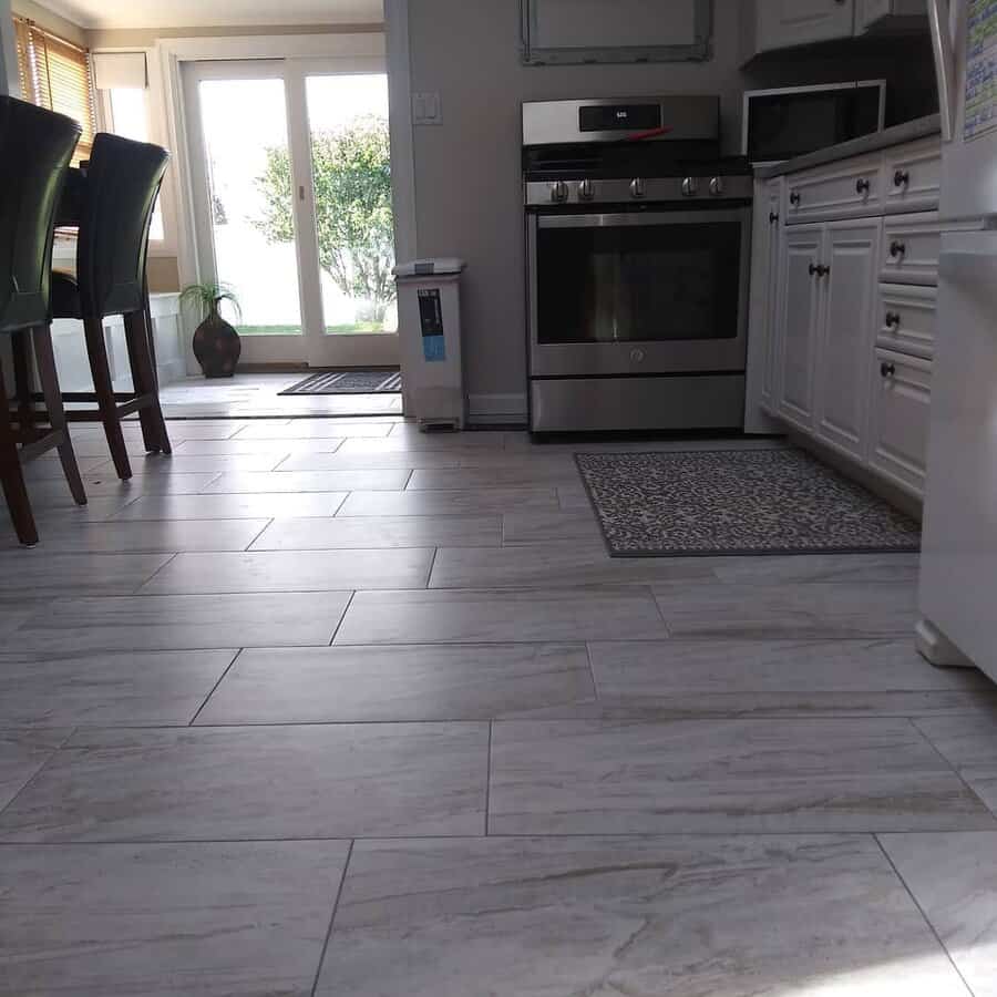 Kitchen with white cabinets, stainless steel appliances, and gray tile flooring, sunlight streaming in through the glass doors