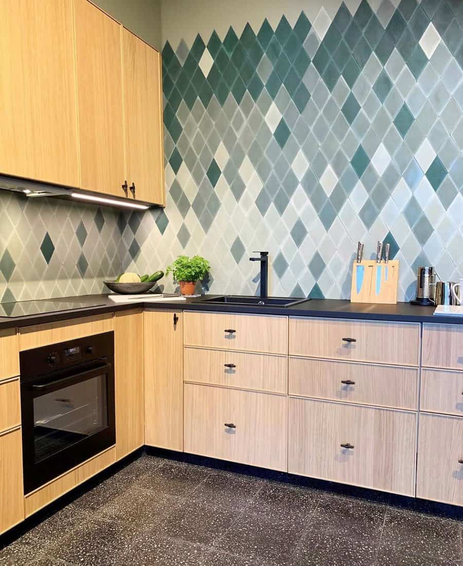 Speckled black tile flooring grounds this modern kitchen, complementing light wood cabinetry and a bold geometric tile backsplash