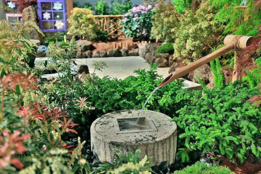 A tranquil Japanese garden with a bamboo water feature, lush greenery, and stone elements