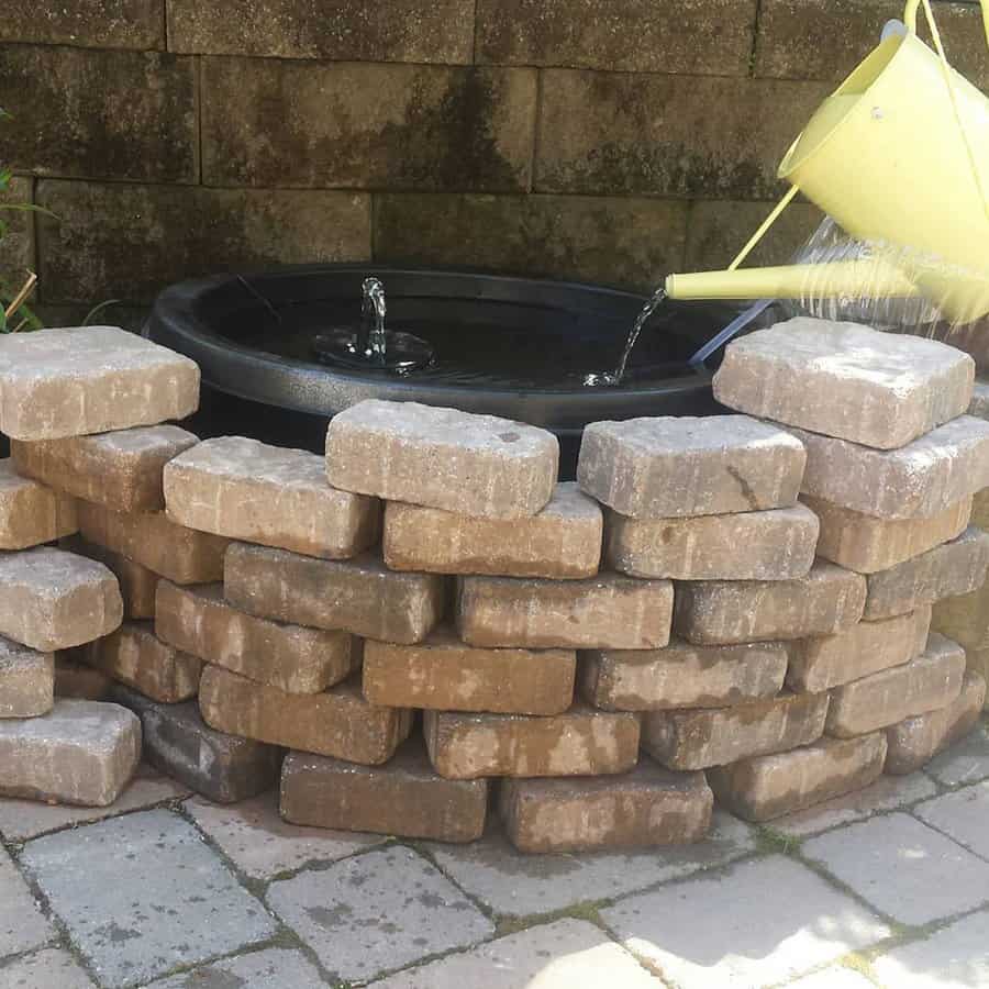 Stone fountain with water can on a brick patio