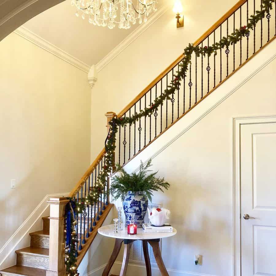 Staircase with garland, chandelier, and a table with a vase and decorations