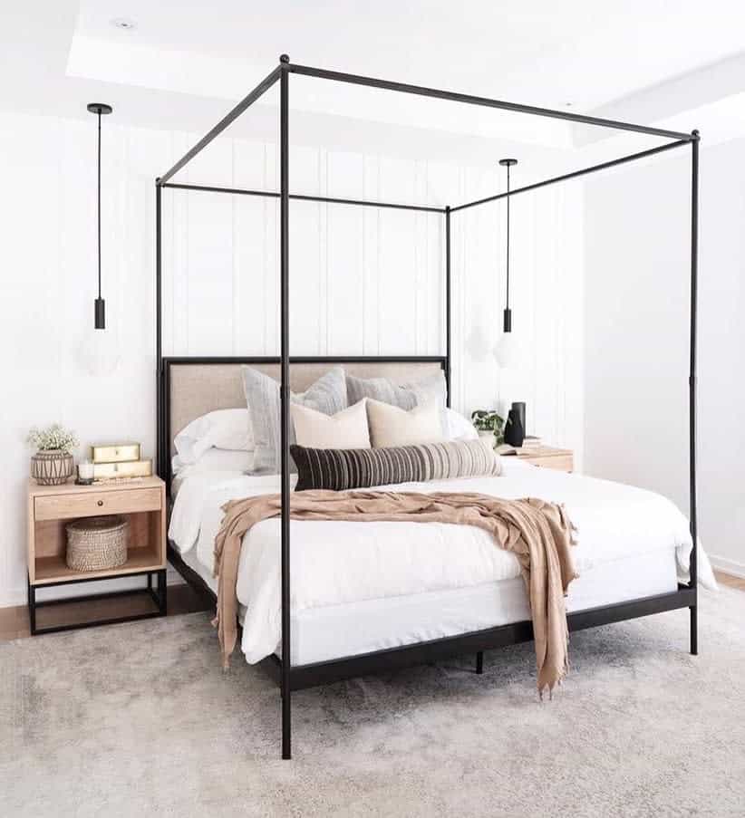 Minimalist bedroom with canopy bed, white and neutral bedding, wooden nightstands, hanging lamps, and a light-colored rug