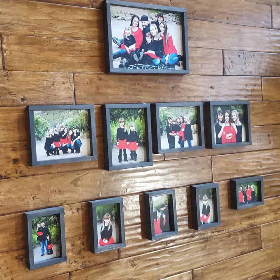 A wooden wall with multiple framed family photos arranged in a grid pattern, featuring groups of people in various poses