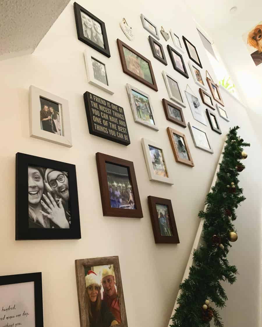 A staircase wall adorned with various photo frames and a Christmas garland along the railing