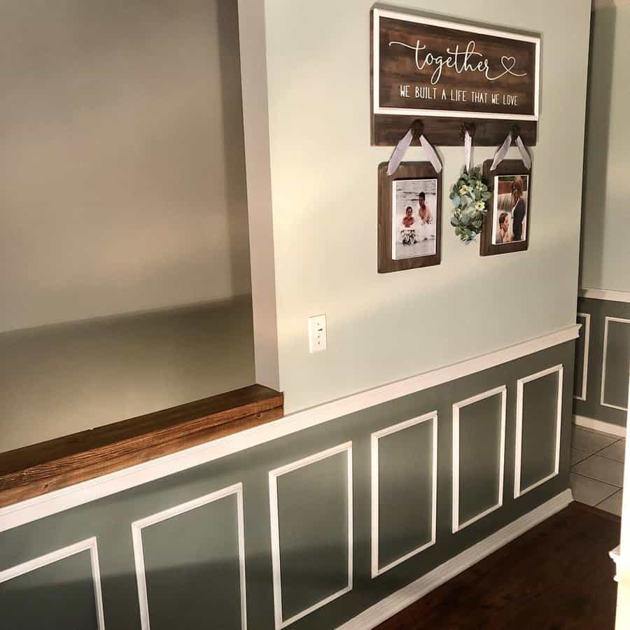 Wall with green paneling and white trim, featuring framed photos, a small wreath, and a wooden sign saying "together" with decorative text