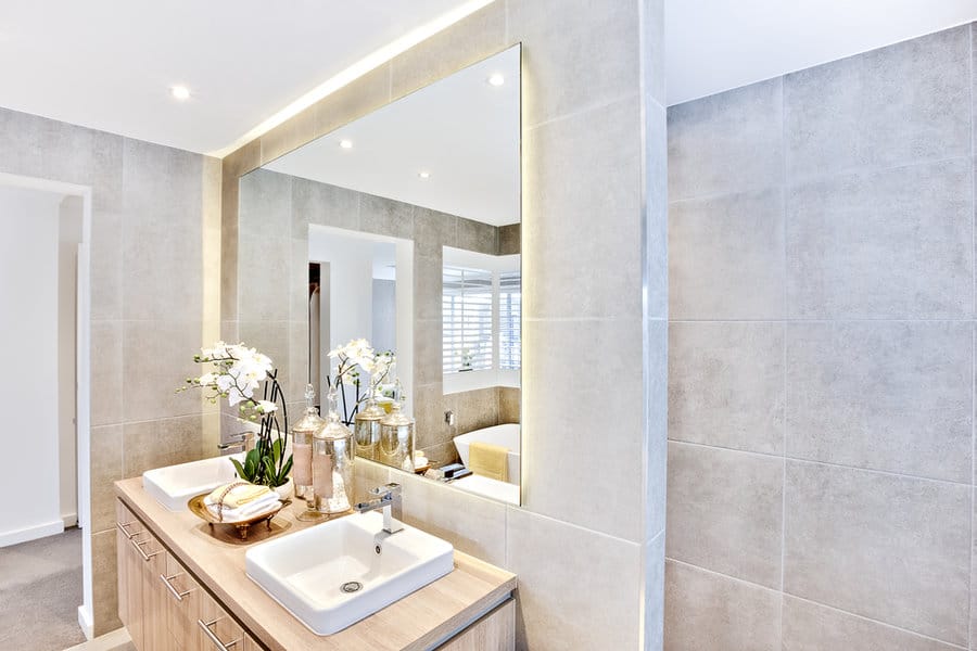 Modern bathroom with double sinks, large mirror, and beige tiles, countertop has potted orchids and decorative items