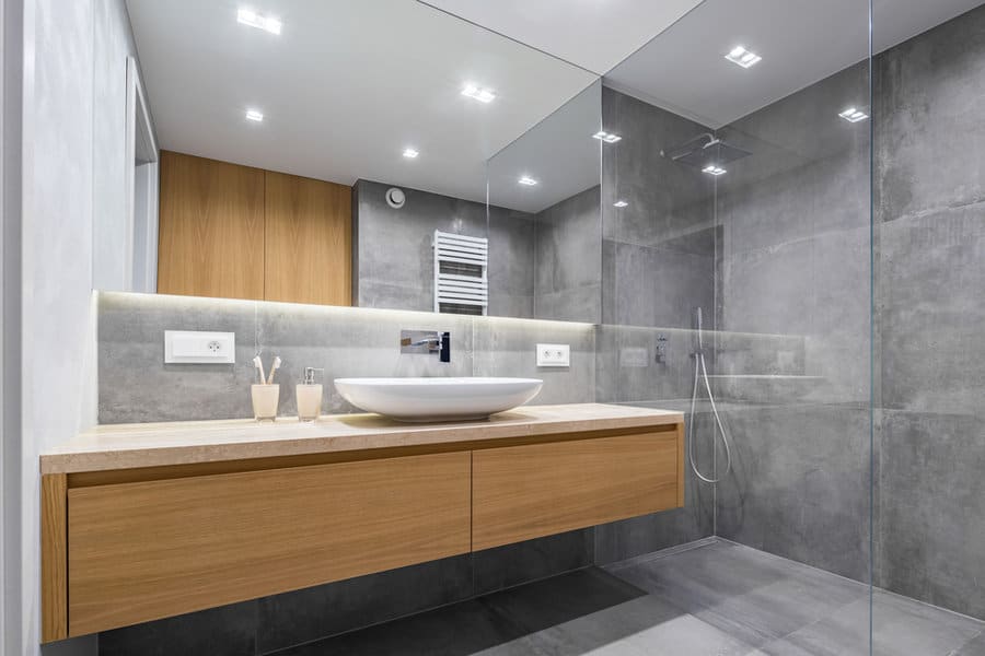 Modern bathroom with a large mirror, wooden vanity, vessel sink, and a glass-enclosed shower; gray walls and ceiling lights enhance the space