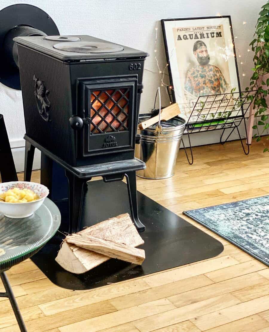 Compact freestanding wood stove with a black hearth pad, warm wooden flooring, and eclectic decor for a cozy yet modern ambiance.