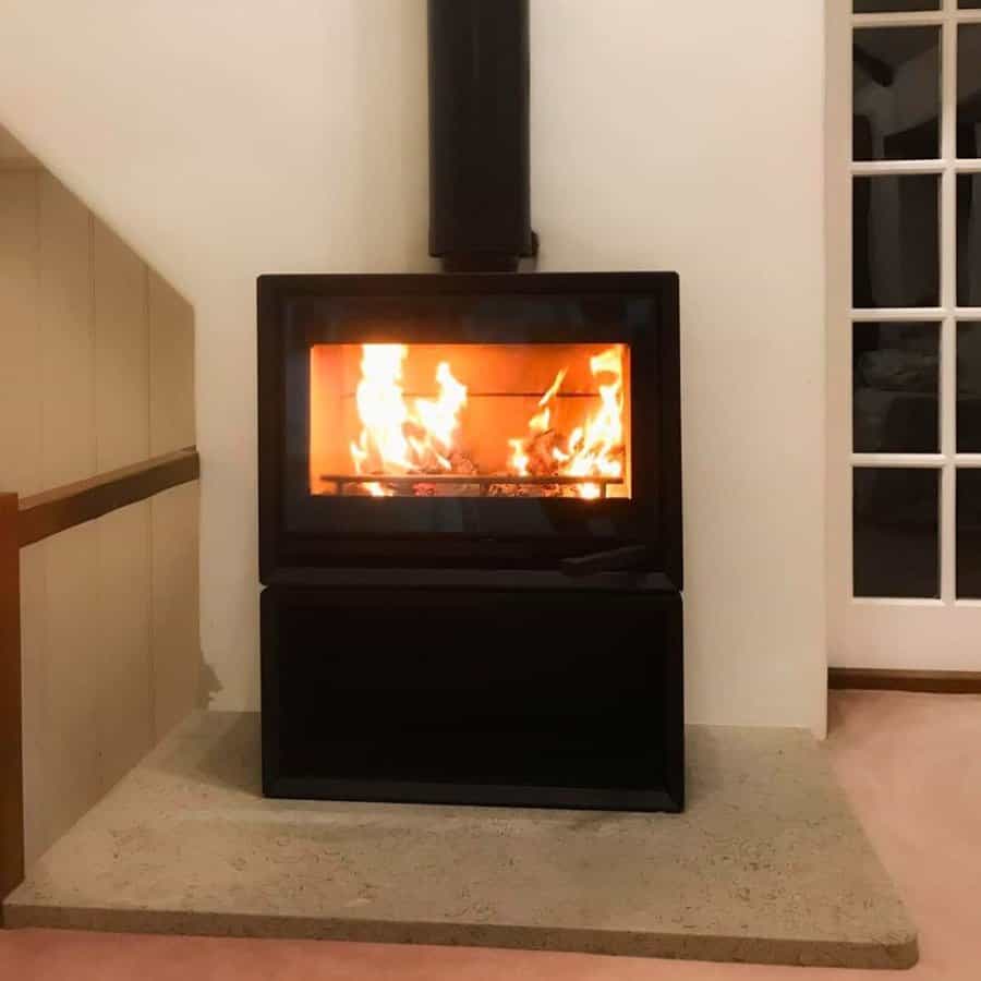 Modern freestanding wood stove with a sleek black design, set on a raised concrete hearth for a minimalist and cozy ambiance.