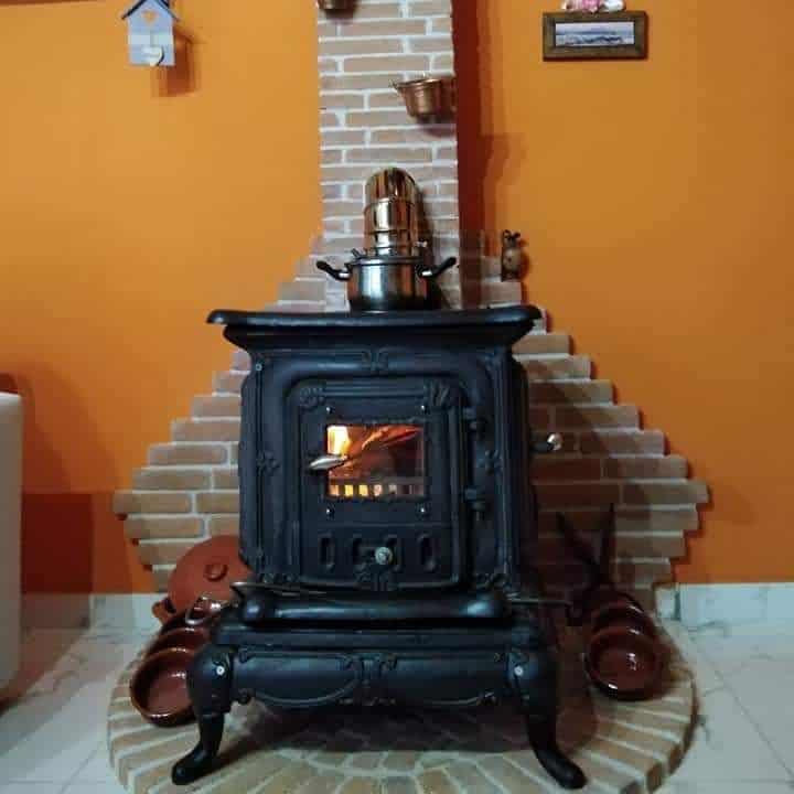 Vintage cast iron wood stove with ornate details, set against a rustic brick hearth and warm orange walls for a cozy, traditional feel.