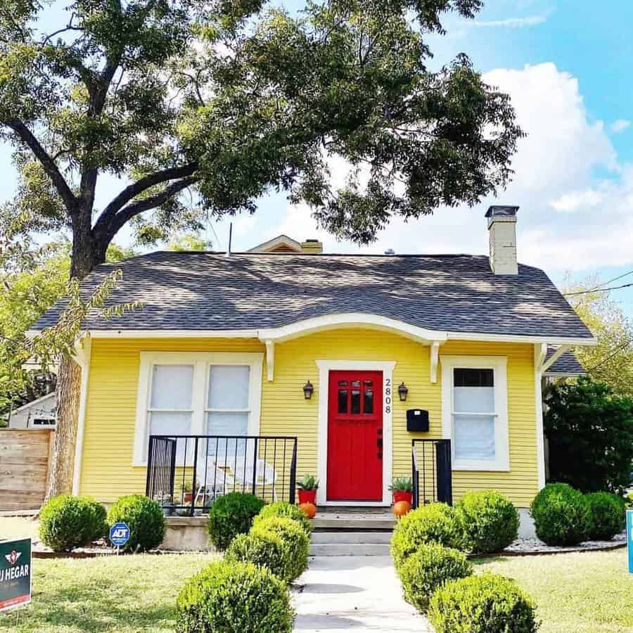 Yellow house with a bright red door and a tree in the front yard