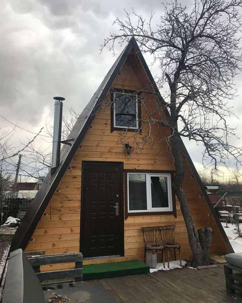 A-frame wooden cabin with a tree next to it