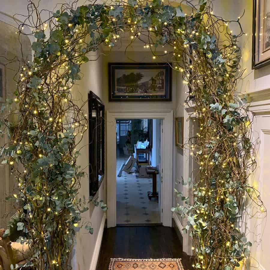 Hallway with a decorative archway made of twigs and greenery adorned with string lights, leading to a room with distant furniture