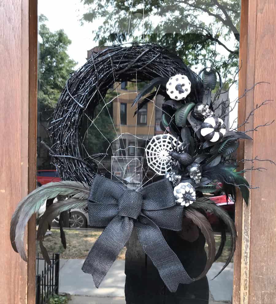 Black Halloween wreath with feathers, ribbons, and skull decorations on a wooden door