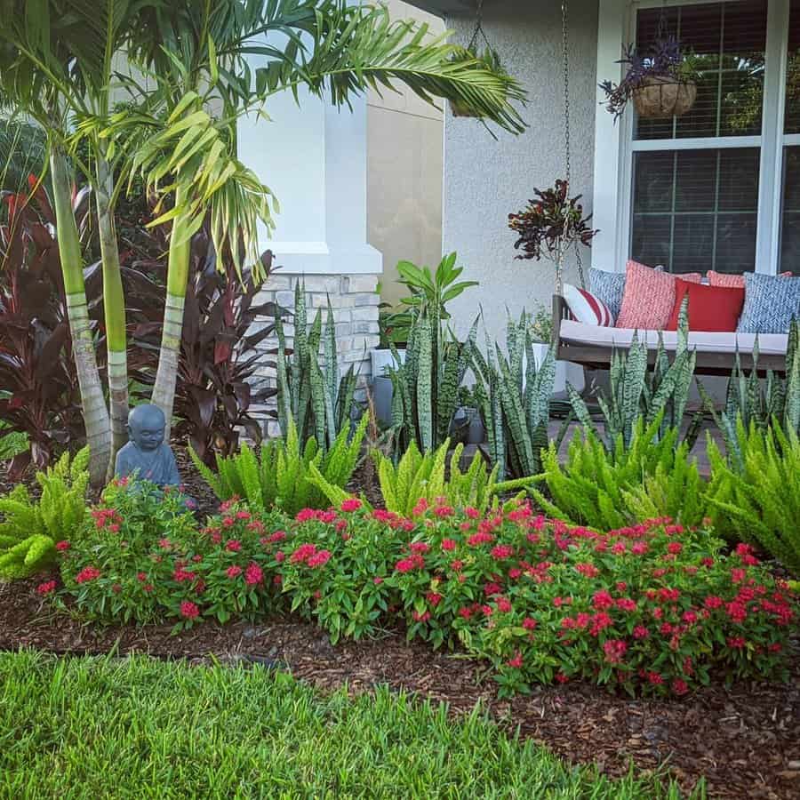 Charming Florida front yard with palm trees, ferns, snake plants, and vibrant red flowers, complemented by a cozy porch swing with colorful cushions