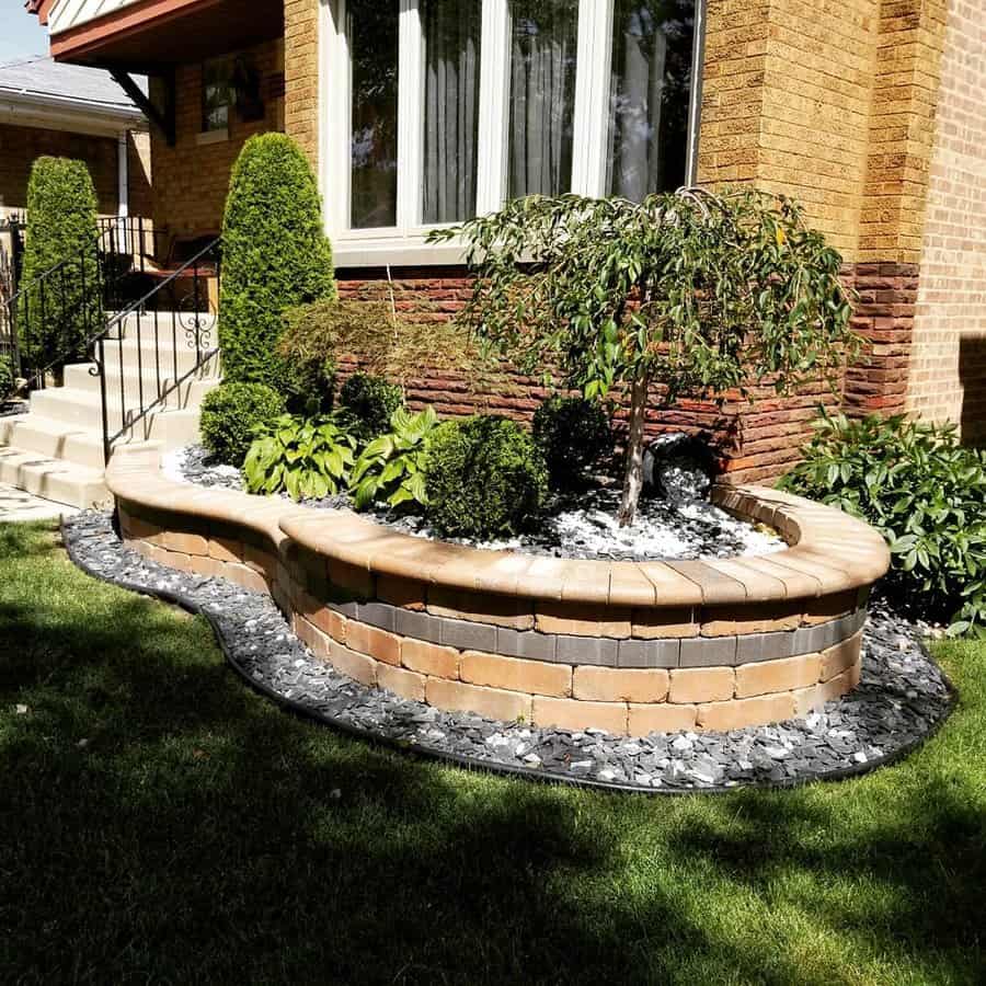 Front yard with a raised brick planter, neatly trimmed shrubs, a small tree, decorative white and black gravel, and lush green lawn