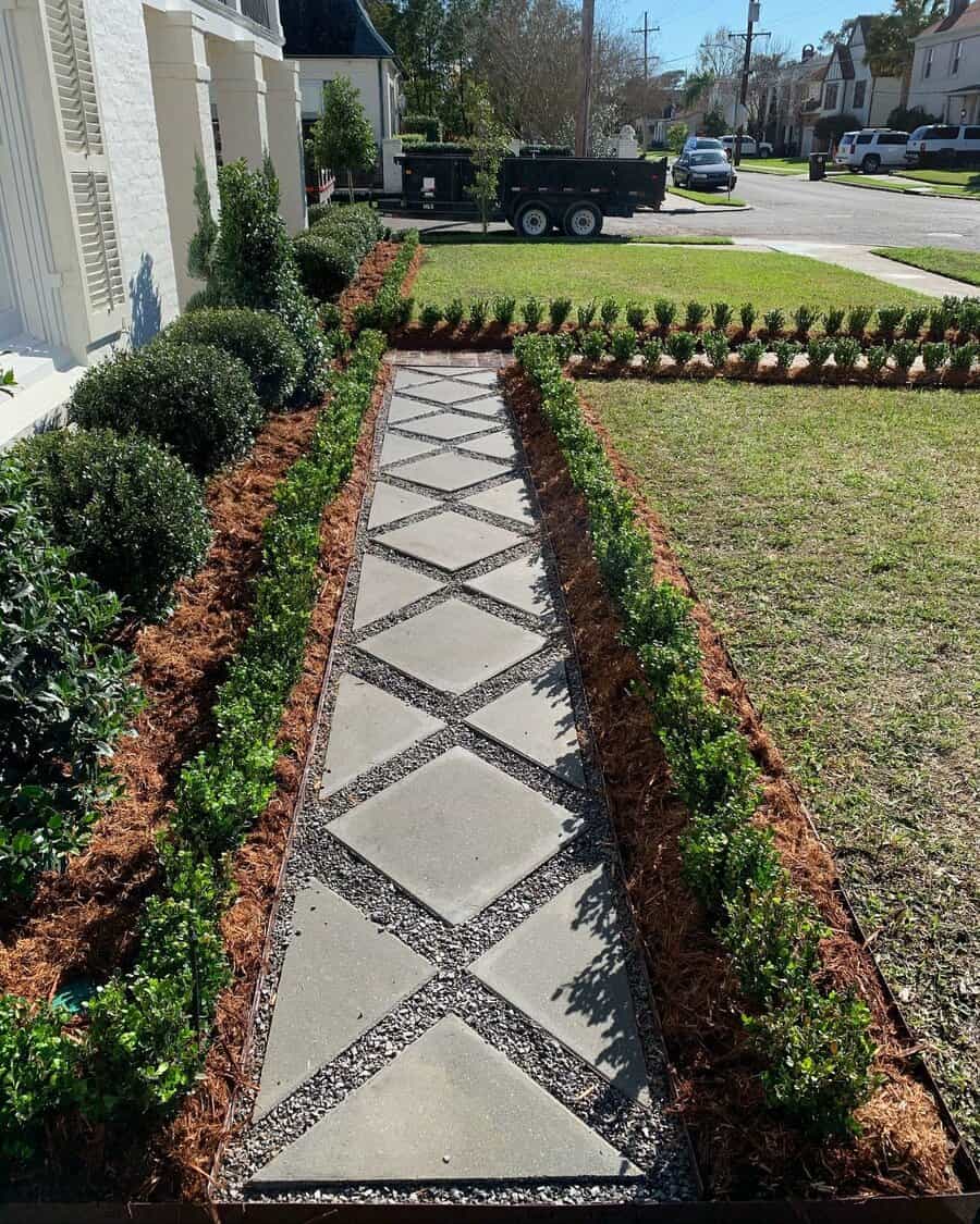 Elegant front yard walkway with diamond-patterned pavers, bordered by mulch, neatly trimmed shrubs, and a well-maintained lawn