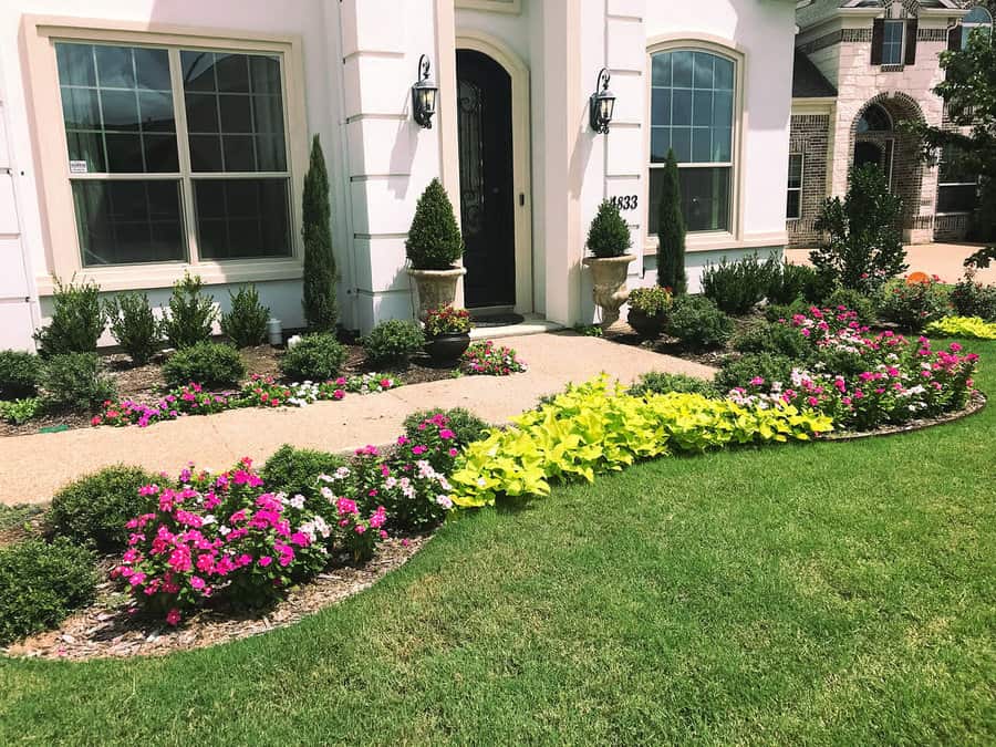 Vibrant front yard design featuring neatly trimmed shrubs, colorful flowers, and a lush green lawn framing a welcoming walkway leading to the front entrance