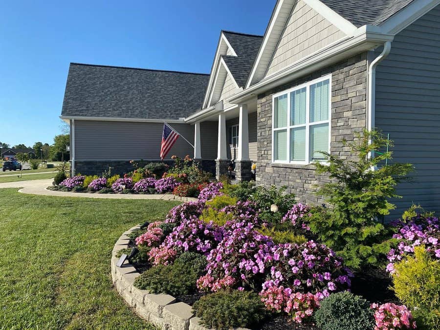 Charming front yard landscaping featuring a variety of colorful flowers, neatly arranged shrubs, and a well-maintained lawn complementing the modern stone façade of the home