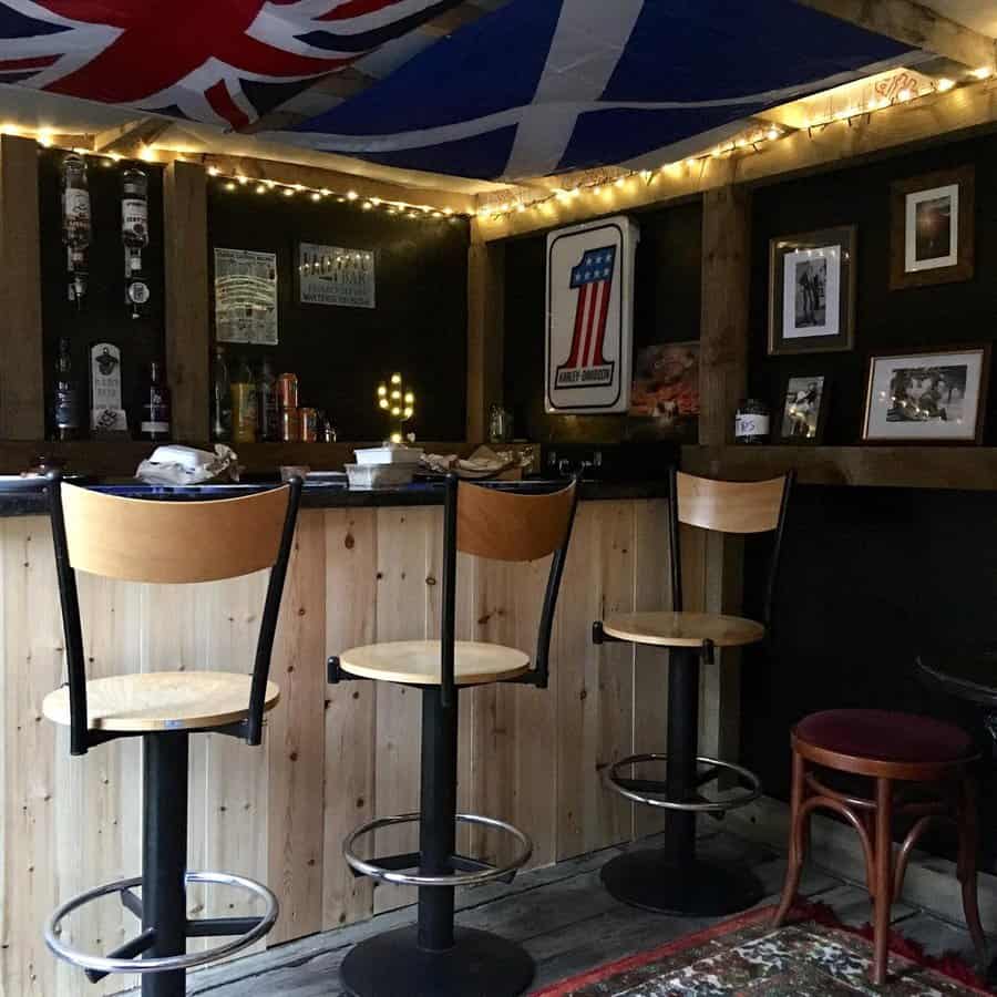 Cozy backyard bar with a wooden counter, string lights, and flag decor, creating a warm pub-like atmosphere for entertaining guests