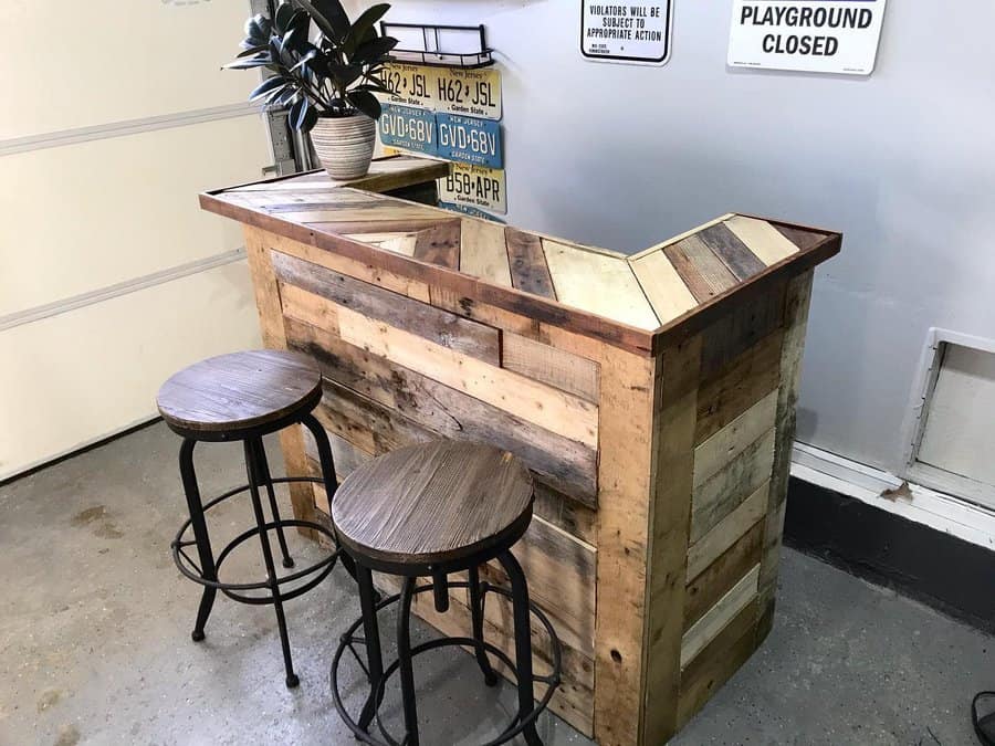 Home bar made of reclaimed wood with two stools, a potted plant on top, and vintage license plates on the wall