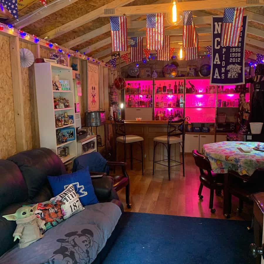 Cozy room with American flags, neon lights, bar area, and couches; decor includes shelves with collectibles and a Grogu plush