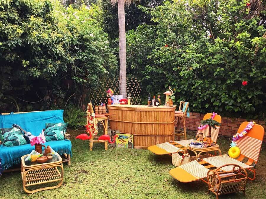 Tropical backyard setting with bamboo bar, colorful lounge chairs, a blue sofa, tropical decor, and lush green plants