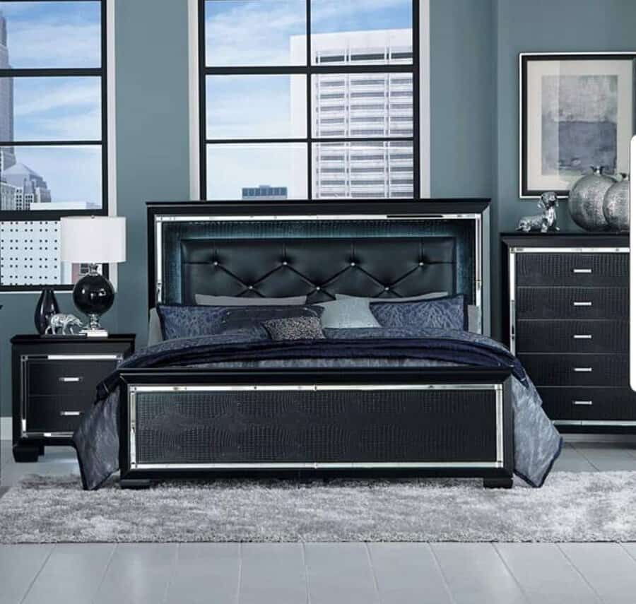 Modern bedroom with a black bed, matching nightstand, dresser, gray rug, and large windows overlooking a cityscape