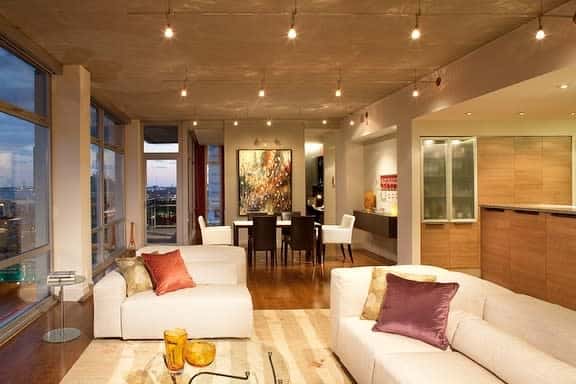 Modern living room with beige sofas, colorful cushions, and a large abstract painting, city view through floor-to-ceiling windows