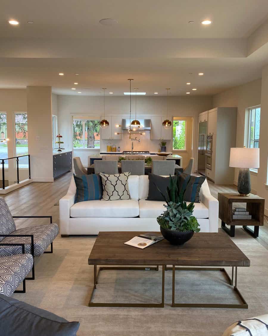 Spacious modern living room with a white sofa, decorative pillows, a wooden coffee table, and a view into a sleek kitchen area