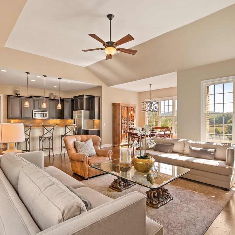 Warm open floor plan with a cozy living area, dark kitchen cabinets, and a sunlit dining space with large windows and elegant decor