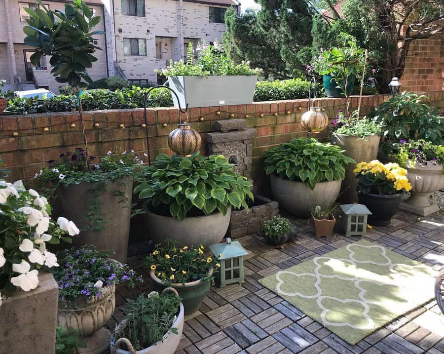 Cozy patio garden with various potted plants, flowers, lanterns, and a small water feature set on a brick and tile surface