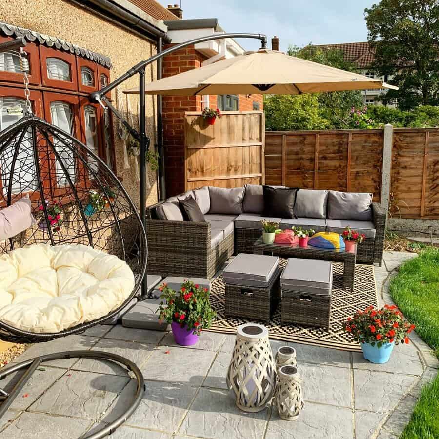 Cozy patio with wicker furniture, cushions, a hanging chair, an umbrella, colorful pots, and lanterns on a stone floor