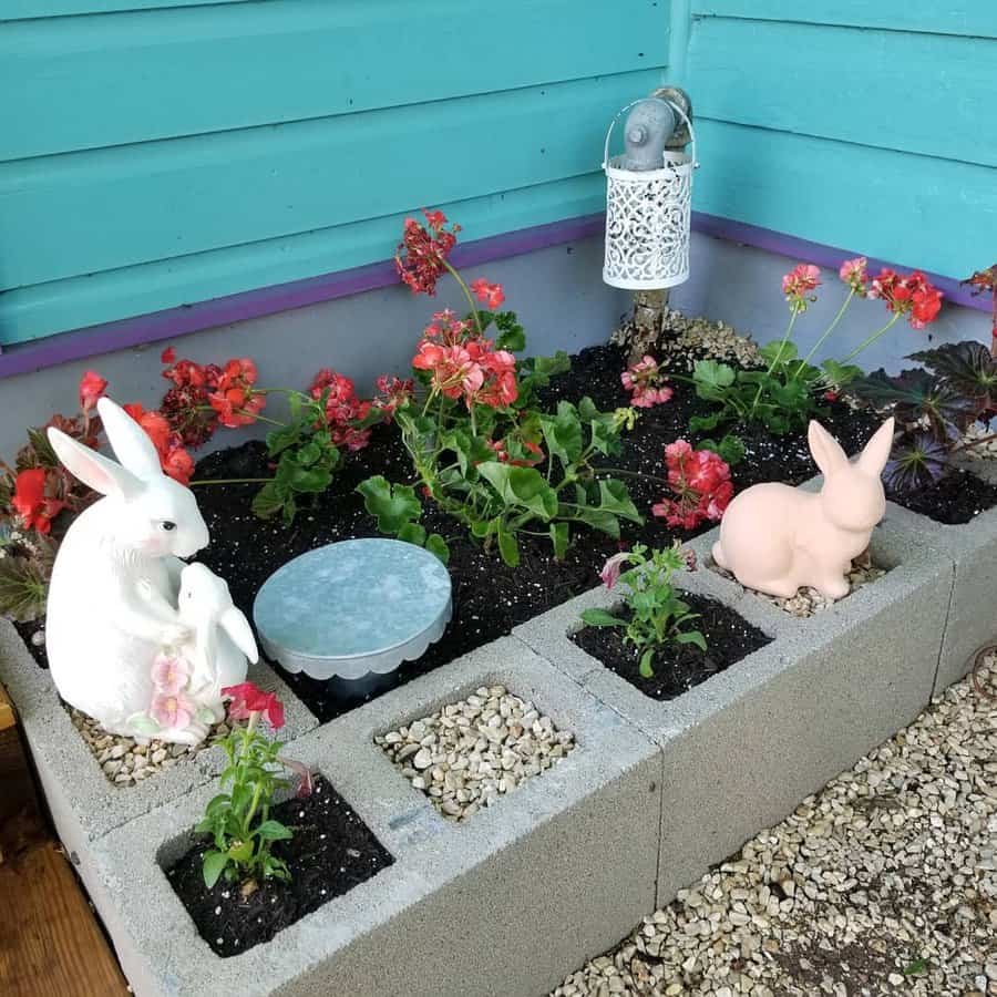 Charming DIY cinder block garden bed with blooming flowers, decorative bunny statues, and gravel accents, creating a cozy and whimsical outdoor space