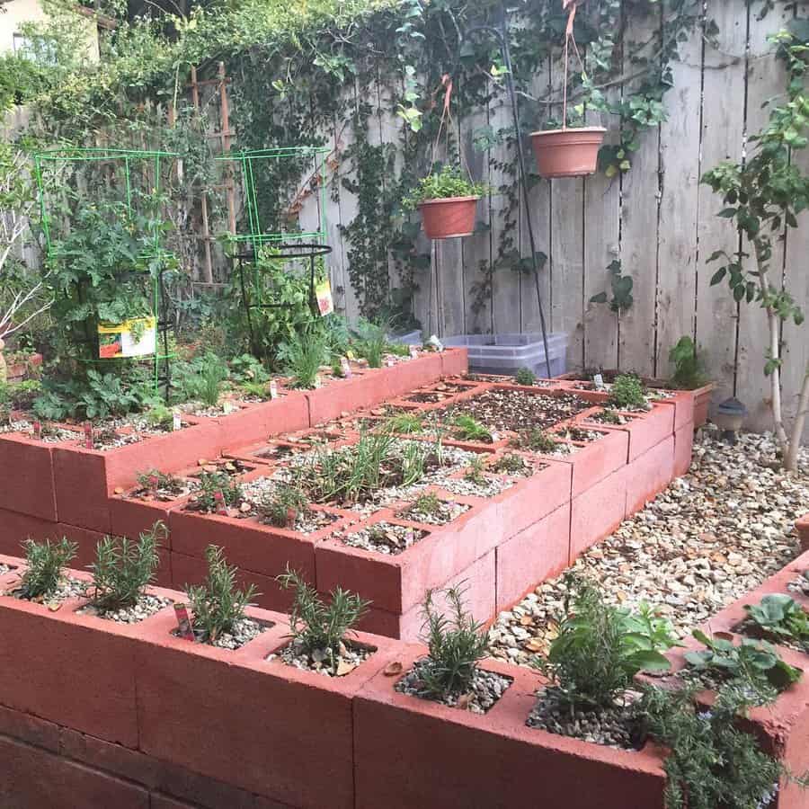 Multi-level DIY cinder block garden bed painted red, featuring herbs, vegetables, and trellised plants, creating a functional and organized backyard space