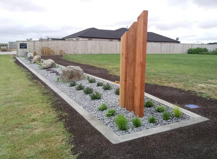 Modern garden design featuring wooden vertical panels, gravel landscaping, boulders, and neatly arranged greenery in a minimalist layout