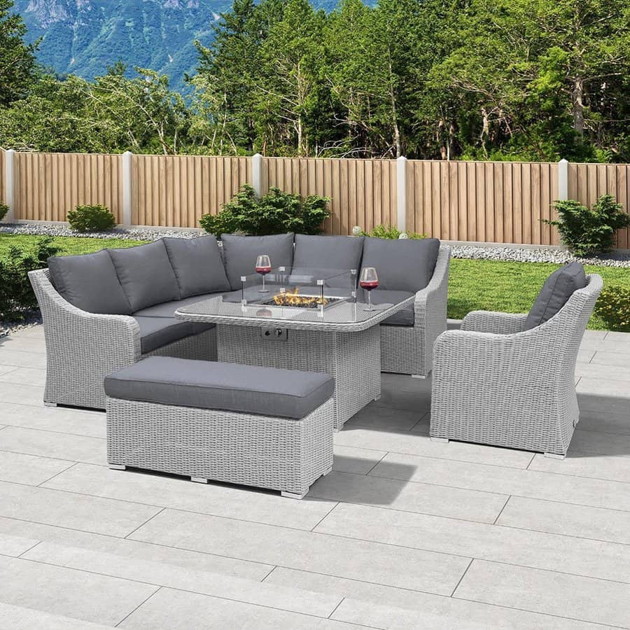 Outdoor patio with gray wicker furniture, including a sectional, a bench, and a glass-top table with wine glasses, mountains in view