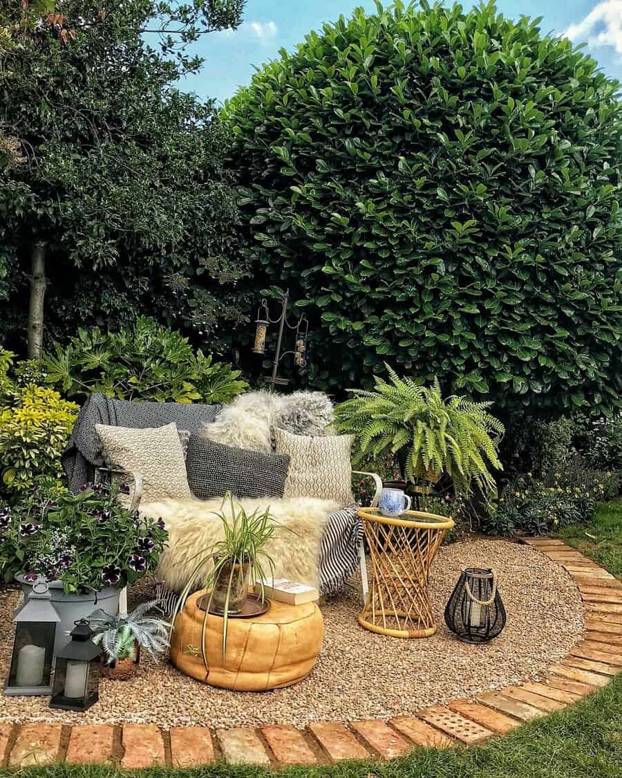 Cozy outdoor seating area with cushions and blanket on a sofa, surrounded by plants and a small table, on a gravel-paved section