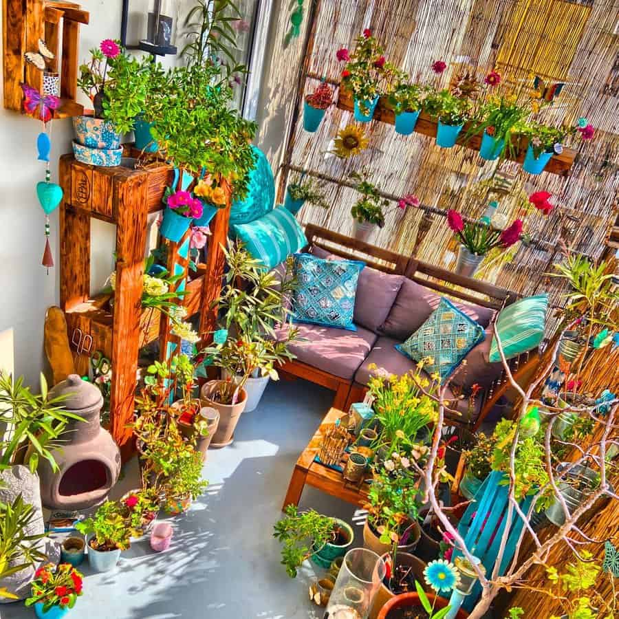 Colorful balcony with plants, vibrant flowers, wooden shelves, a cushioned sofa, and decorative pots creating a cozy, lively atmosphere