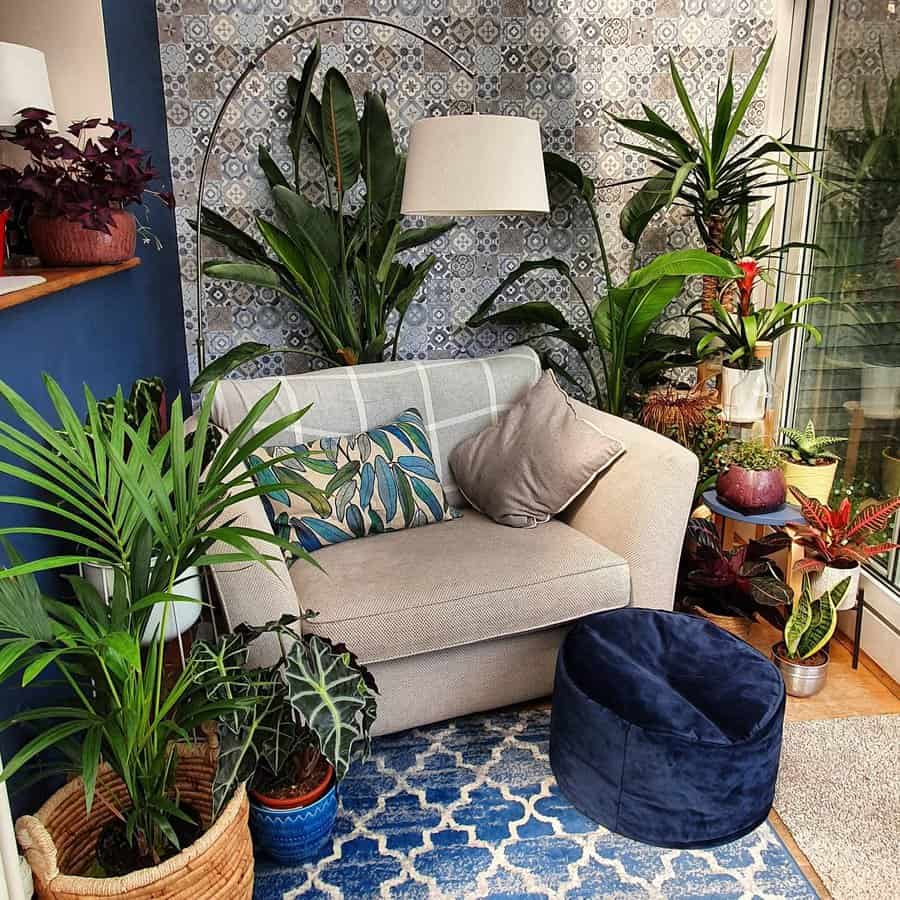 Cozy corner with a beige armchair, vibrant plants, a blue pouf, patterned wallpaper, and a geometric rug