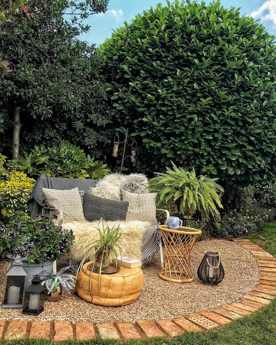 Cozy garden nook with a wicker sofa, cushions, a small table, and plants surrounded by lush greenery and a large leafy tree